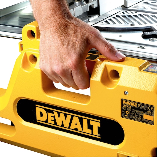 A close-up of a person's hand gripping the yellow handle of a DEWALT DW743N tool, with the DEWALT logo clearly visible on the side. The tool has a textured metal surface and product information label.
