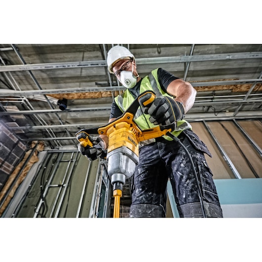 A construction worker wearing a safety vest, gloves, and a hard hat uses a yellow DEWALT corded mixing drill (DWD241) inside a building under construction.