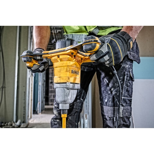 A person wearing work gloves and protective clothing operates a DEWALT electric mixer drill in a construction setting.