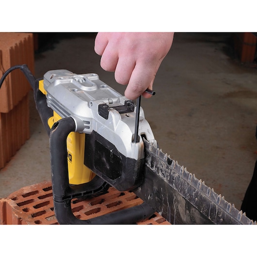 A close-up of a person using a hex key to adjust a DEWALT power saw, positioned on a brick surface.
