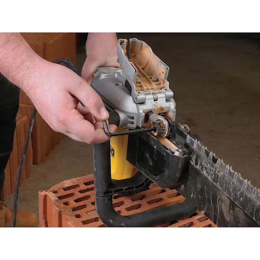 A person uses an Allen key to adjust or maintain a DEWALT electric masonry saw, positioned on a stack of bricks.