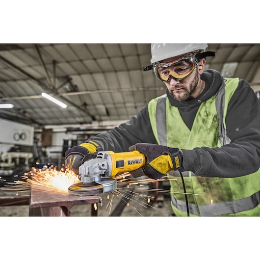 A construction worker wearing safety gear uses a DEWALT angle grinder (model DWE4036) to cut metal, producing sparks in an industrial workshop.