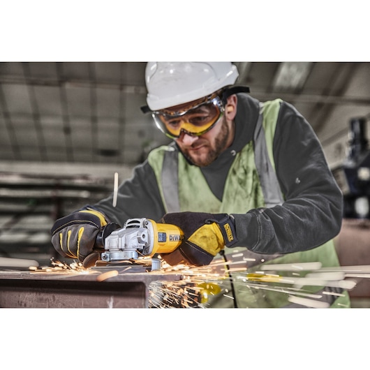 A person wearing a safety vest, gloves, and a hard hat is using a DEWALT angle grinder (model DWE4036) to work on a metal surface, producing sparks in an industrial setting. The person's face is obscured.