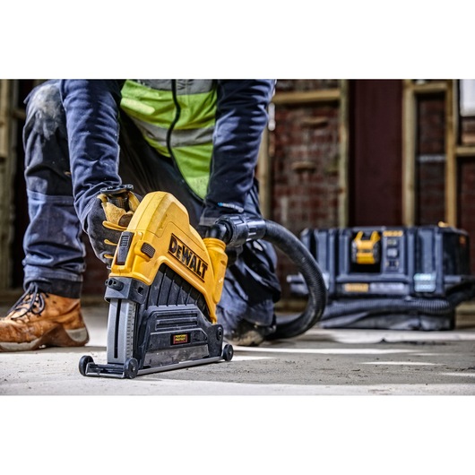 A person using a DEWALT plunge saw attached to a dust extraction hose, working on a construction site with a DEWALT storage case in the background.