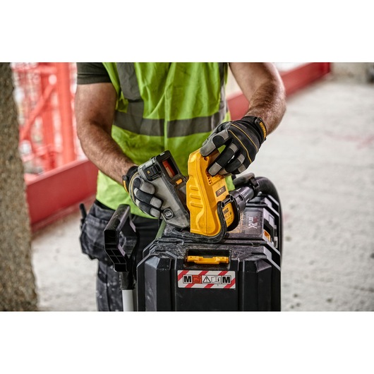 A person wearing a high-visibility vest and work gloves is holding a DEWALT tool and battery, assembling them on top of a black equipment case at a construction site.