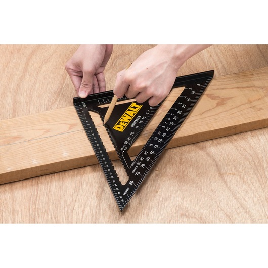 Person using a DEWALT DWHT25228-0 black triangular rafter square to mark a straight line on a wooden plank with a pencil.