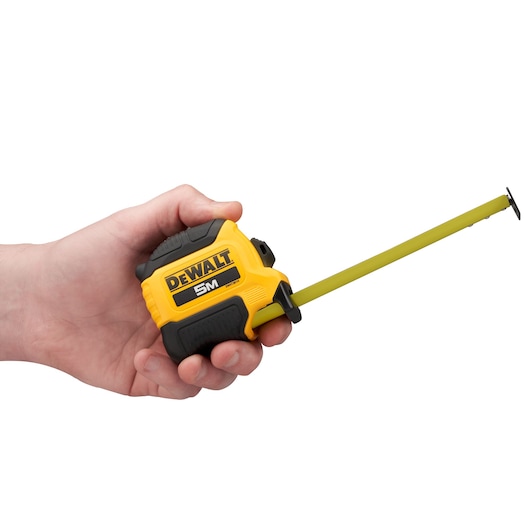 A hand holding a yellow and black DEWALT 5m tape measure with the tape partially extended.