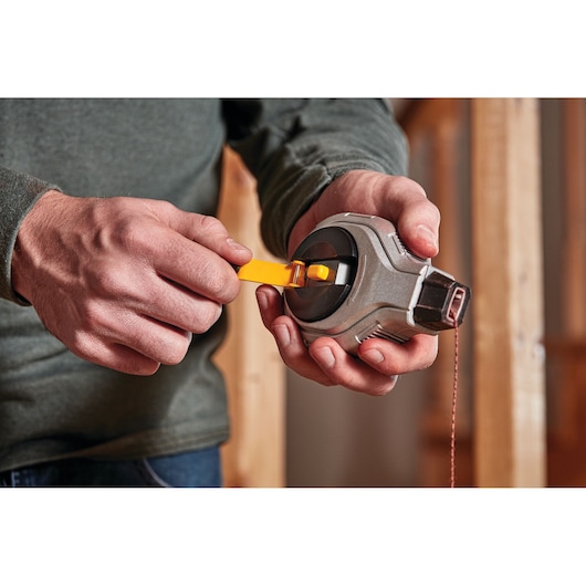 A person is holding a DEWALT chalk line reel and using a yellow handle to wind the string.