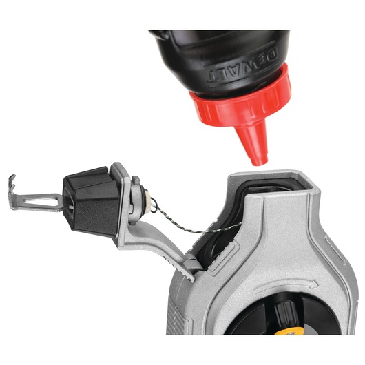 Close-up image of a DEWALT chalk line tool with its compartment open, being refilled with chalk powder from a bottle with a red nozzle.