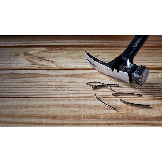 A DEWALT claw hammer resting on a wooden surface with several bent nails lying nearby.
