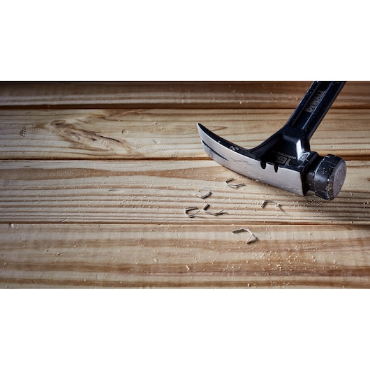 A close-up of a DEWALT claw hammer with a black handle resting on a wooden surface, surrounded by wood shavings.