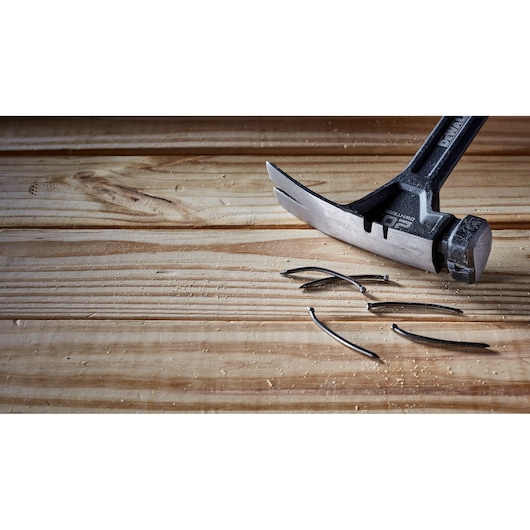 A DEWALT claw hammer resting on a wooden surface next to several bent nails.
