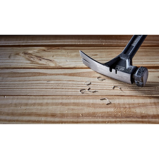 A DEWALT claw hammer is shown removing nails from a wooden surface, with wood shavings and small metal pieces scattered around.
