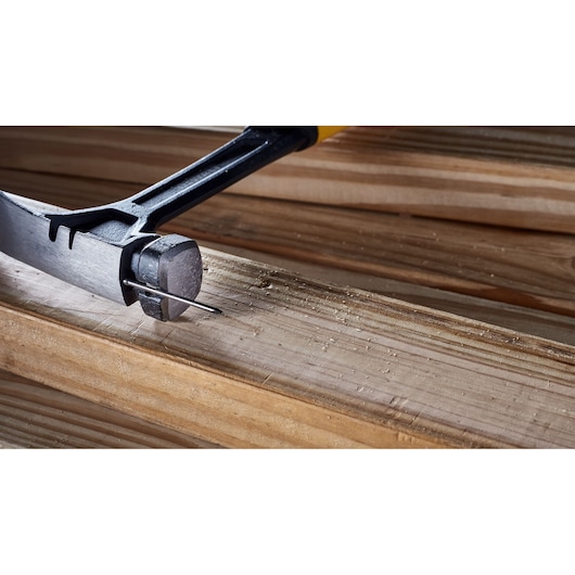 Close-up of a DEWALT hammer extracting a metal nail from a wooden plank.