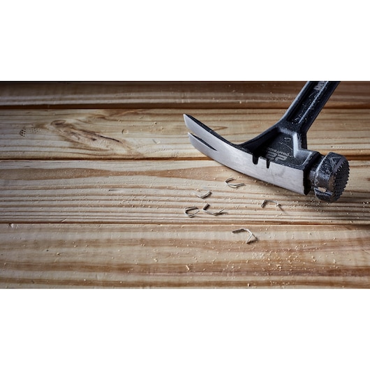 Close-up of a DEWALT claw hammer head resting on a wooden surface with wood shavings and small bent nails around it.