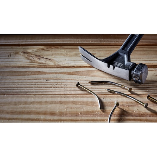 A DEWALT claw hammer is resting on a wooden surface next to several bent nails.