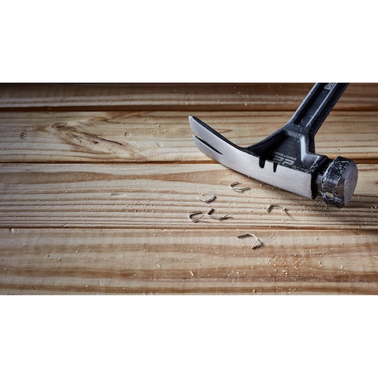 A DEWALT claw hammer with a metal head and black handle is lying on a wooden surface, surrounded by wood shavings and small nails.