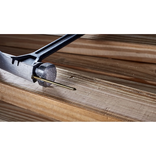 A close-up view of a DEWALT hammer driving a nail into a wooden plank.