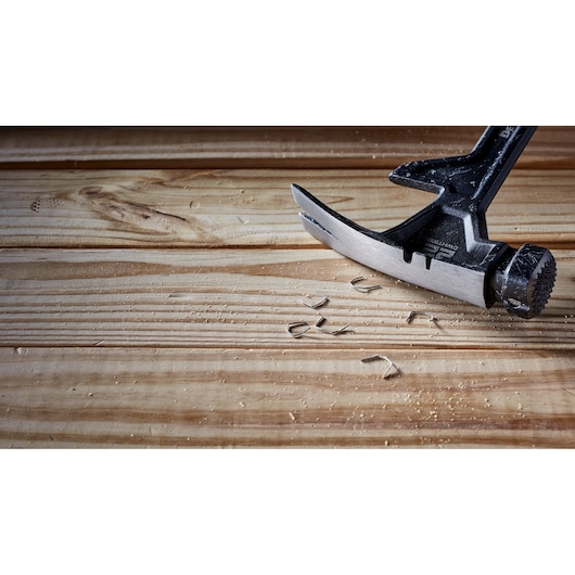 A DEWALT claw hammer with a black handle is resting on a wooden surface, with wood shavings and nails visible nearby.
