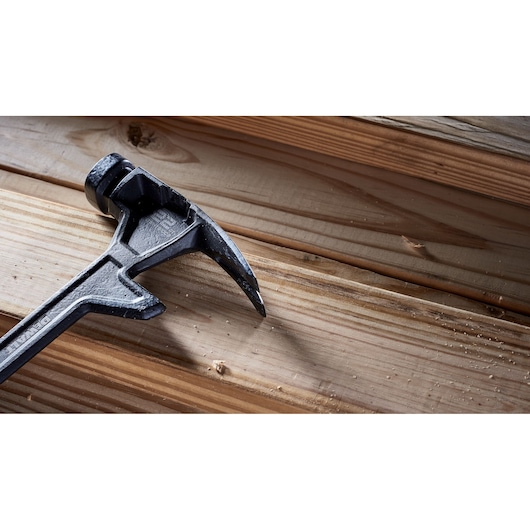 Close-up of a DEWALT claw hammer resting on wooden planks, showing its textured metal head and handle.