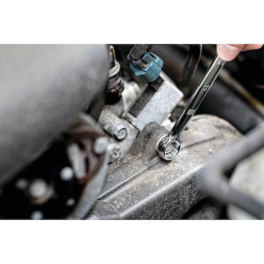 A close-up view of a person using a DEWALT ratcheting wrench to tighten a bolt on a metal engine part.