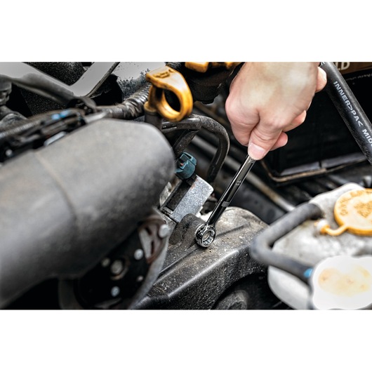 A close-up view of a hand using a DEWALT ratcheting wrench on a bolt within an engine compartment, demonstrating automotive repair or maintenance.