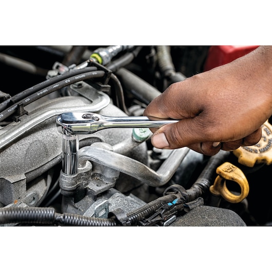 A hand using a DEWALT ratchet wrench to tighten or loosen a bolt on a car engine.