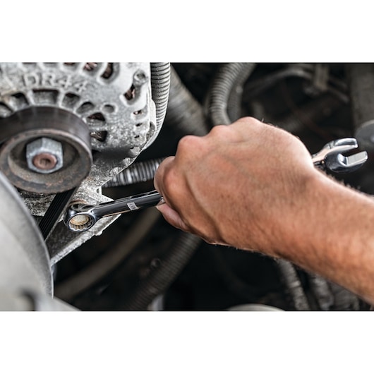 A close-up of a hand using a DEWALT ratcheting wrench to tighten or loosen a bolt on a vehicle engine part.