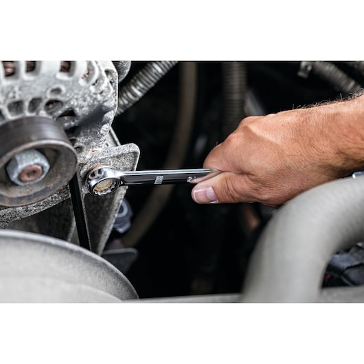 Close-up of a person's hand using a DEWALT ratcheting combination wrench to tighten or loosen a bolt on an engine part.