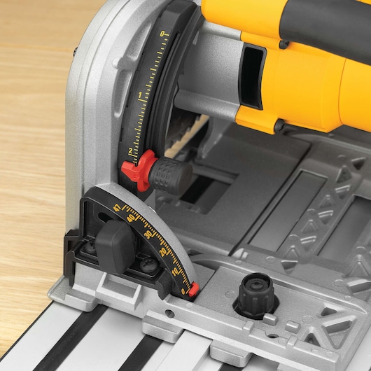Close-up view of a DEWALT track saw adjustment mechanism, showing detailed angle and depth measurement scales, adjustment knobs, and part of the saw's yellow and black housing on a wooden surface.