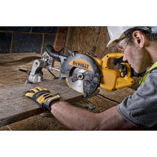 A person wearing gloves and a safety helmet operating a DEWALT DWS773 miter saw, cutting a piece of wood in a workshop.