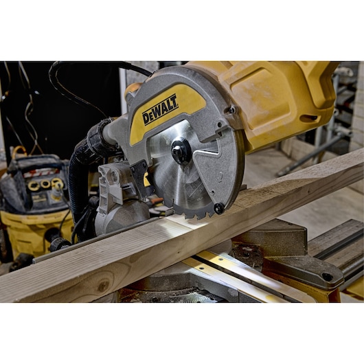 A DEWALT DWS777 mitre saw cutting a wooden plank in a workshop setting.
