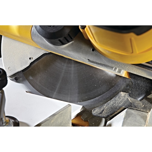 Close-up view of a DEWALT DWS778 miter saw cutting a piece of wood, showing the circular blade in operation.