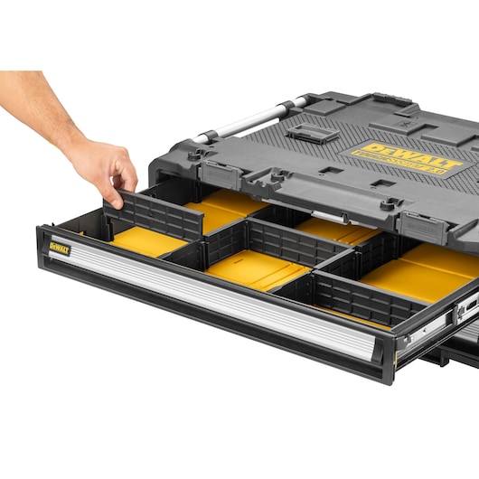 A DEWALT modular tool storage case with a partially open drawer featuring customizable compartments, a yellow interior, and a side handle. A hand is adjusting one of the dividers.