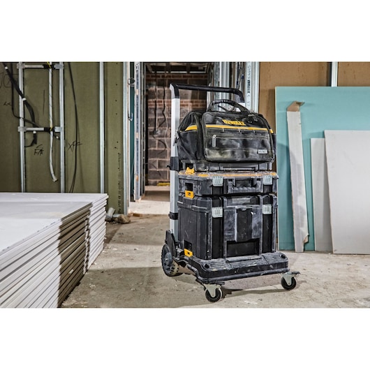 DEWALT mobile tool storage system with three stackable black organizers and a tool bag on top, placed on wheels in a construction site.
