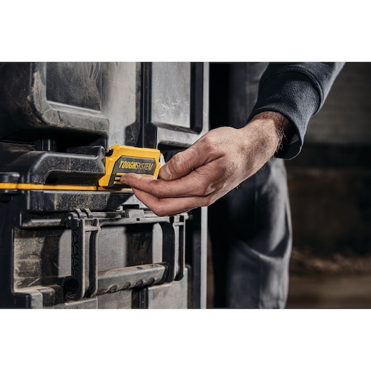 A close-up of a person's hand operating the yellow latch of a DEWALT TOUGHSYSTEM storage box.
