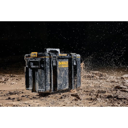 A rugged DEWALT ToughSystem 2.0 tool box covered in mud, shown being dropped onto a muddy ground with mud splashing around it, highlighting its durability and resistance to harsh environments.