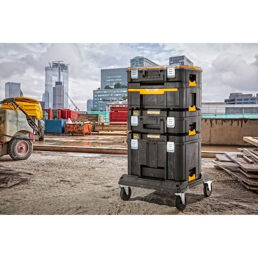 Stacked DEWALT black and yellow tool storage boxes on a wheeled cart at a construction site, with modern city buildings in the background.