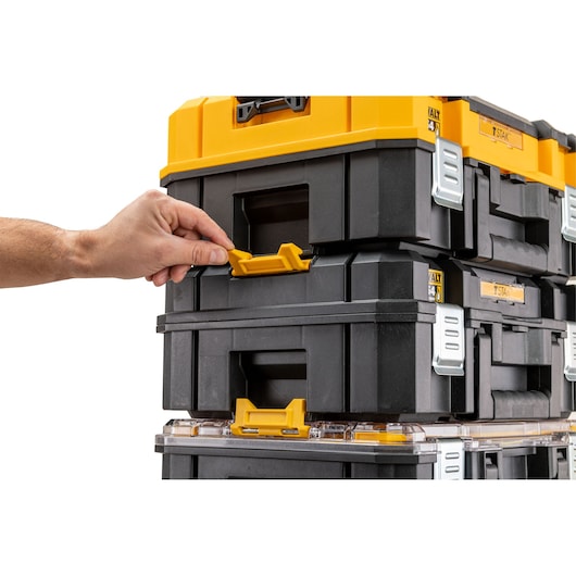 A close-up of a hand unlocking a yellow latch on a stack of black and yellow DEWALT TSTAK storage boxes.