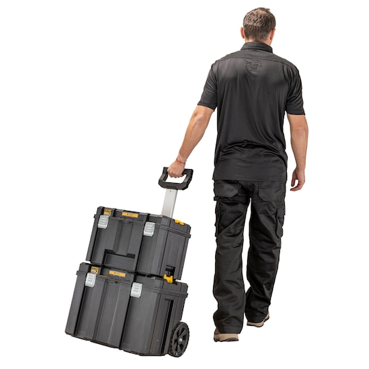 A person is pulling a stack of two DEWALT black toolboxes with wheels and a telescopic handle. The toolboxes are designed for portability and storage of tools.