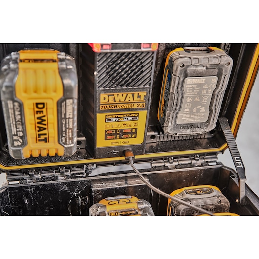 Close-up view of a DEWALT ToughSystem 2.0 storage box with several DEWALT lithium-ion batteries and a charging station inside. The batteries are organized and connected to the charger within the portable box.