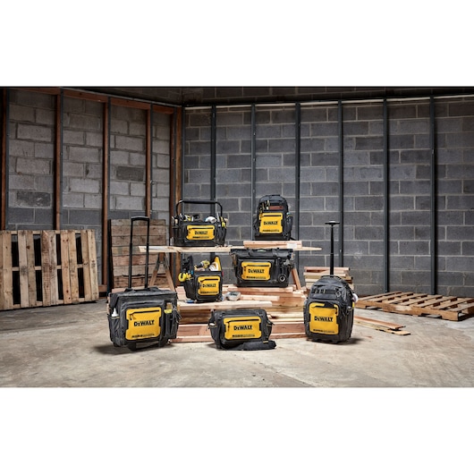 Several DEWALT tool bags and cases in various sizes are displayed on wooden pallets in an industrial warehouse setting with concrete block walls.