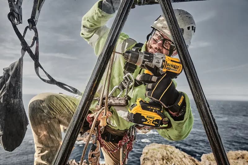 Photo of worker using DEWALT drill, SKUs DCD996P2, DCD996P2-QW, outdoors with safety gear near sea.