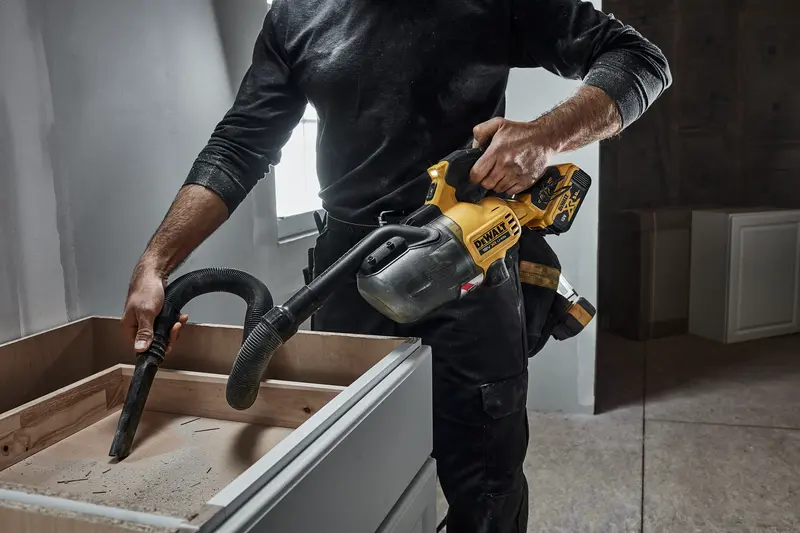 Photo of DEWALT DCV501LN handheld vacuum cleaning dust from cabinet, construction setting, product in use.