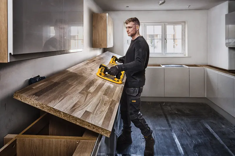 Photo of person using DEWALT DCE592B photography tool in kitchen installing wooden countertop.