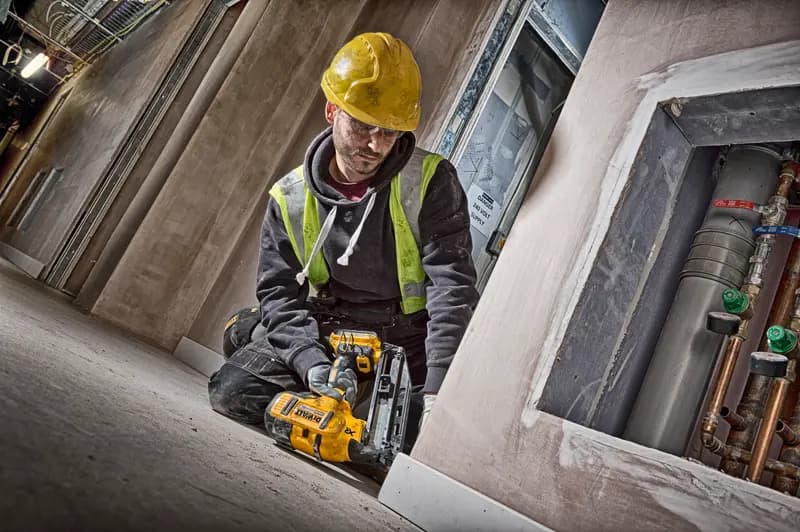 Worker using a DEWALT DCN660N nailer on a construction site, wearing a yellow hard hat and safety vest.