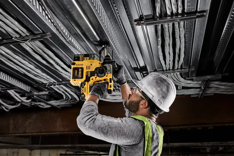 Photo of worker using DEWALT rotary hammer DCH273P2, DCH273P2-GB on ceiling pipes, indoor worksite.
