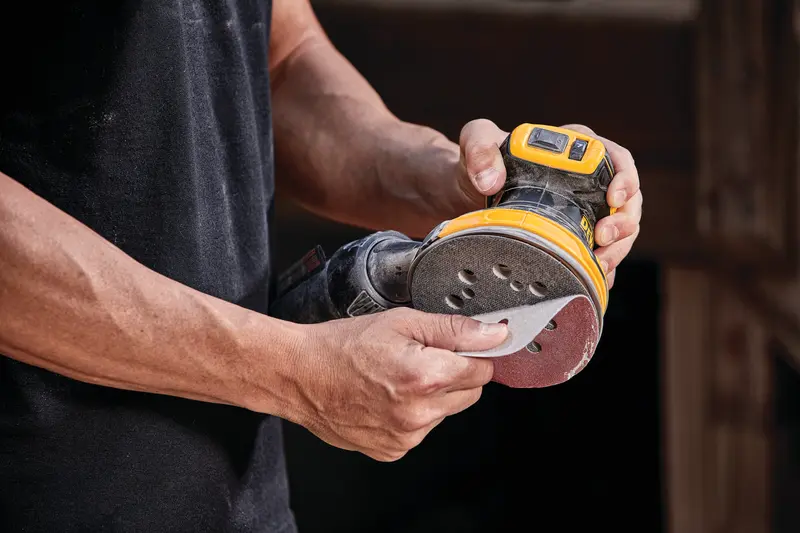 Photo of DEWALT DCW210B sander in use, person attaching sanding disc, handheld tool, closeup view.
