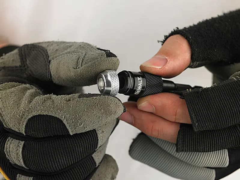Photo of DEWALT DT71507 bit holder in use, held by gloved and bare hands, black and silver tool close-up.