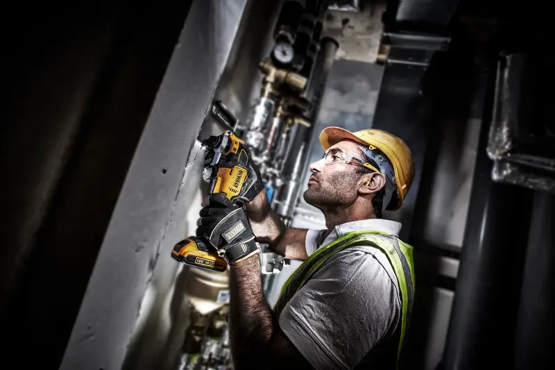 Photo of worker using DEWALT DCS355D2 cordless oscillating tool on industrial site, wearing safety gear.